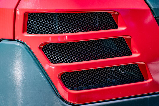 Abstract industrial texture featuring a vibrant red fiberglass cowl panel built with three parallel dark ventilation airflow screens