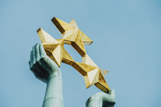 View of the golden stars held aloft by the statue at the top of the Freedom Monument against a clear blue sky in Riga, Latvia.