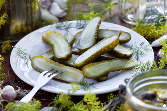 Traditional pickled cucumbers, pickled using the natural fermentation method, on a plate, close-up viewPickled cucumbers with dill flowers, garlic, and horseradish, cut in half, on a plate, close-up. 