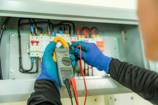 Electrician Testing Circuit Board: A close-up shot shows an electrician wearing blue gloves and a black sleeve, meticulously testing a complex electrical circuit board with a clamp meter.