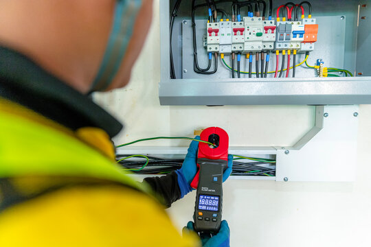 Electrician Testing Electrical Panel: An electrician in safety gear uses a clamp meter to test an electrical circuit breaker panel, ensuring safety and functionality.
