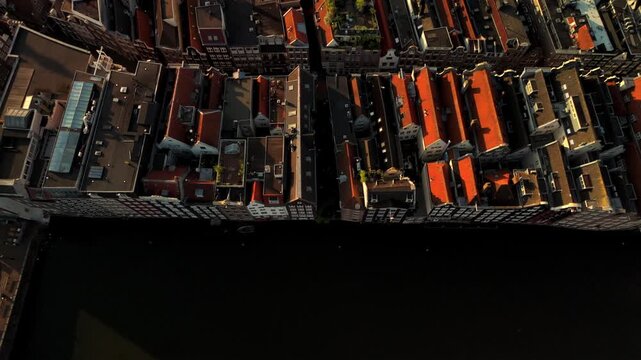 Drone glides along an Amsterdam canal showing terracotta rooftops above and dark water below with a moored boat