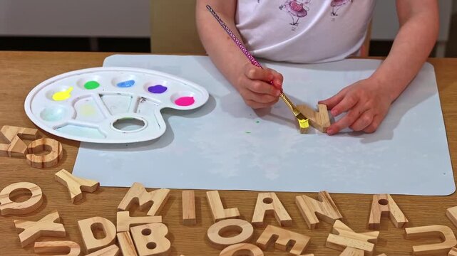 Creative child doing arts and crafts, coloring wooden alphabet blocks with acrylic paint. Letter N