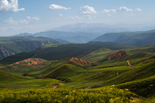View of Arashan ko'li surrounded by rolling green hills and distant mountains under a blue sky in Pop District, Namangan Region, Uzbekistan.