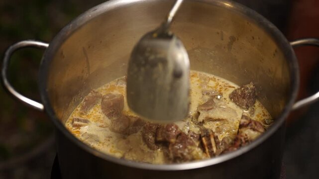 Traditional thai food, Meat pot stew cooking spoon creamy broth beef kitchen metal food preparation with tender chunks in savory dairy base, ladle handle, steam, rustic homemade dinner closeup