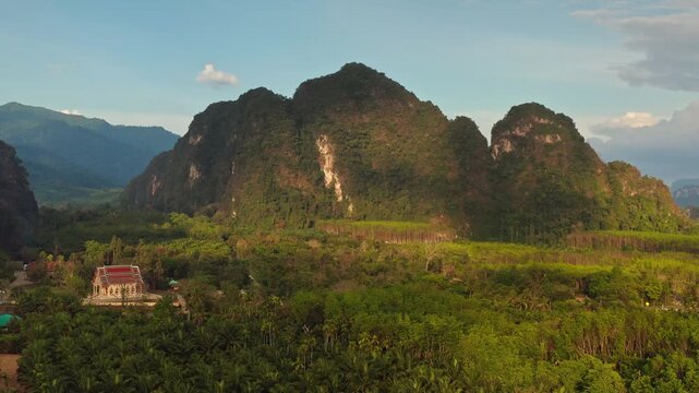 Ancient Buddhist temple standing amidst lush green tropical jungle and towering limestone karsts, capturing serenity and natural beauty of Khao Sok National Park in Thailand. Aerial view drone flight