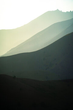 View of Arashan Lake surrounded by rolling mountain silhouettes fading into the distance at sunset in Pop District, Namangan Region, Uzbekistan.
