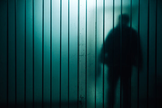Mysterious silhouette shadow behind frosted glass panel conveying isolation and suspense