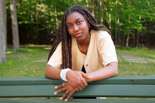 Calm young Black woman with long braids leaning on a green park Bench.