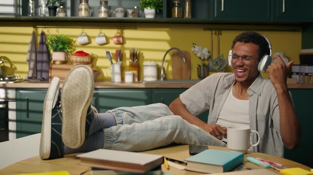Carefree African American man dancing in headphones at home kitchen happy male student listening music during study break enjoying song audio sound moving relaxed teen guy having fun after homework