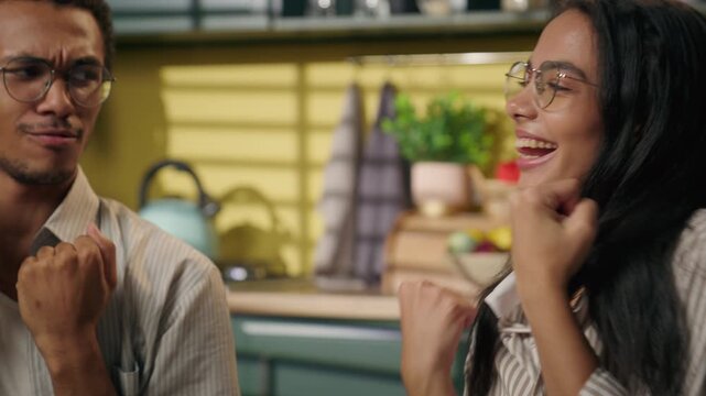Happy African American guy and Latina girl celebrate exam pass at home kitchen dancing together multiracial high school friends studying success carefree gen z teenagers having fun moving indoors