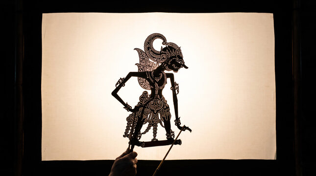 Traditional Javanese wayang kulit shadow puppet silhouette held against illuminated screen during live dalang performance, Indonesian UNESCO intangible heritage