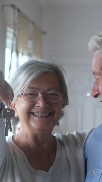 Cheerful elderly couple embracing and smiling while holding the keys to their new home. Proud homeowners celebrating a fresh start, real estate purchase, and successful investment together
