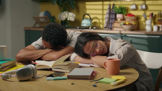 Tired African American guy and girl sleeping on kitchen table home after studying exhausted high school students fall asleep over homework boring study fatigue overwork sleepy gen z teens nap indoor