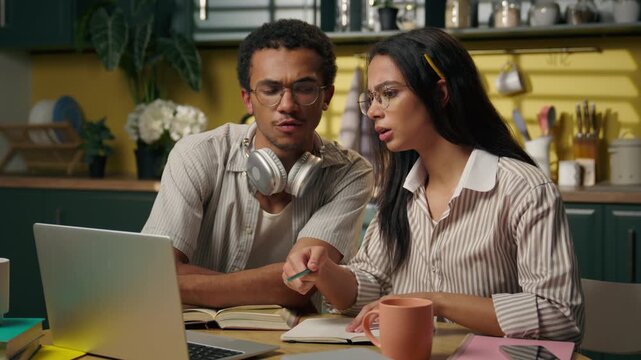 Multiracial African American man and Latina woman studying together at home using laptop at table college students writing homework online class distant education teamwork learning teens pc at kitchen
