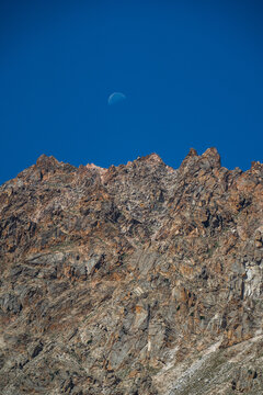 View of the rugged mountain peaks near Arashan Lake under a clear blue sky with a visible crescent moon in Pop District, Namangan Region, Uzbekistan.