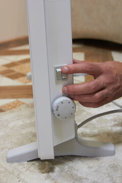 A man's hand turns on an electric convector heater, close-up. Concept of energy saving, heating season and comfort in winter.