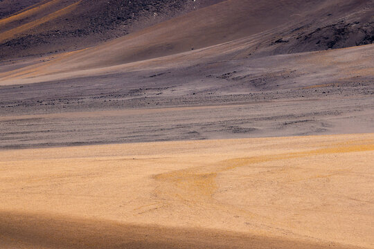 View of the vast, arid landscape of La Pacana Caldera with textured volcanic soil and rolling desert dunes under clear light in San Pedro de Atacama, Antofagasta, Chile.