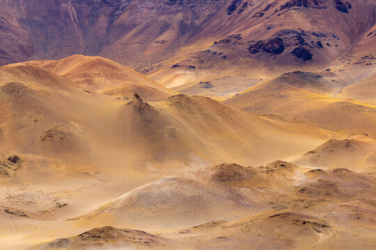 View of the arid volcanic landscape of La Pacana Caldera with undulating golden hills and rugged terrain in San Pedro de Atacama, Antofagasta, Chile.
