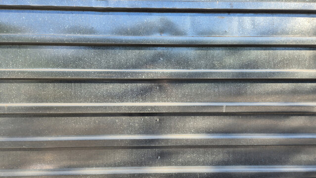 A close-up shot displays a horizontal corrugated metal fence panel with a shiny, galvanized steel texture.