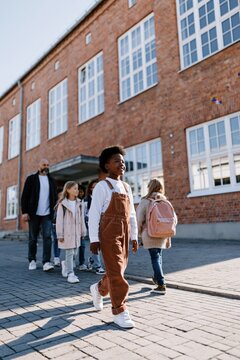 Child leading group walking past brick school building with backpacks and adult chaperone for back to school banner and education background