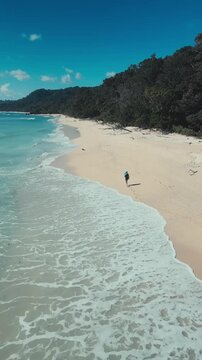Solo beach wanderer. Walking alone on sandy coast. Secluded individual exploring sunlit shoreline. Solitary trekker traversing sandy shores with reflective mood.Vertical video