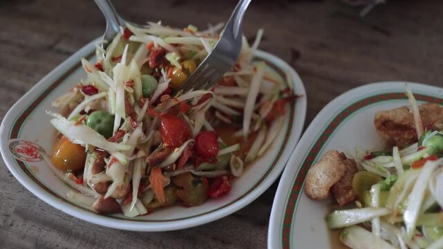 Mixing Fresh & Spicy Thai Papaya Salad (Som Tum) with Fork & Spoon in Asian Street Restaurant. Traditional Northeast Isaan Food in Bangkok Thailand