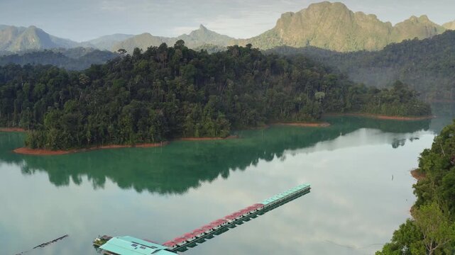 Cheow Lan Lake in Khao Sok National Park, Thailand, floating bungalows complex amidst lush rainforest and dramatic limestone mountains, reflecting in turquoise water. Aerial view drone flight panorama