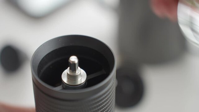 Hand adding coffee beans to coffee grinder from glass cup. Concept of coffee preparation and home coffee brewing