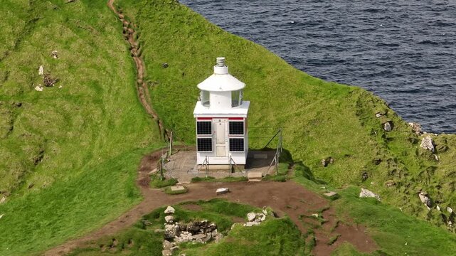 Aerial tracking shot with a pan left movement of the iconic Kallur Lighthouse. Located on the cliffs near Tr&oslash;llanes on the Faroe Islands, showcasing rugged coastal beauty.