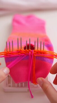 Close up of hands using a darning loom to mend a colorful sock.