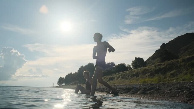 Carefree happy teenagers at sea throwing stones into water and enjoying life. Tall slim boy in swimwear throwing stones into sea at sunset with teenage girl in swimwear. enjoying youth and life