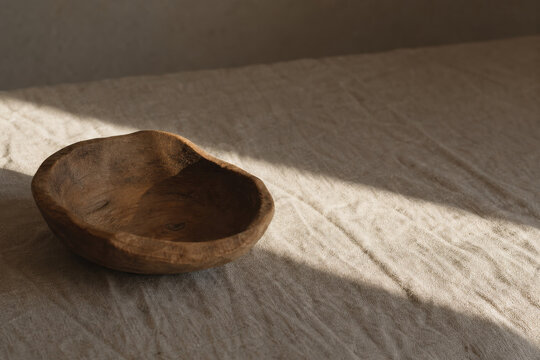 Minimalist still life with a hand-carved wooden bowl on a beige linen tablecloth.