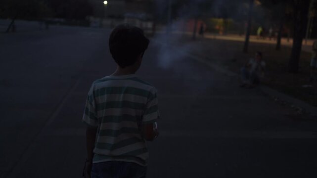 Young boy watching a firecracker explode on the street at dusk, celebrating the 4th of july in a suburban neighborhood with family enjoying the festive pyrotechnics
