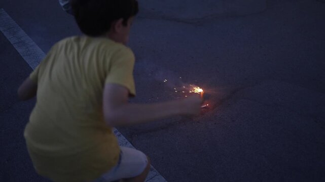 Children lighting small fireworks fountain on asphalt parking lot during twilight celebration, sparks flying and smoke creating a festive and exciting atmosphere for boys
