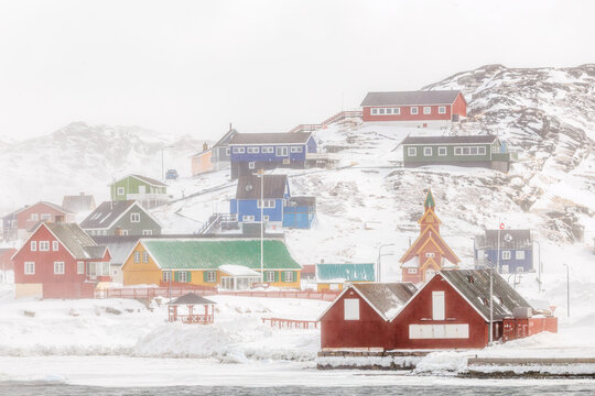 Fredens Church and colorful Greenlandic houses on a snowy hillside during heavy winter snowfall, Paamiut, Sermersooq, Greenland