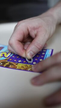 Vertical screen Close up of hand scratching lottery ticket with coin revealing hidden symbols during game of chance hoping for lucky jackpot and instant cash prize
