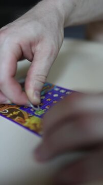 Vertical screen Close up of hand scratching colorful lottery ticket with coin revealing hidden symbols hoping for instant cash prize jackpot and lucky winning moment
