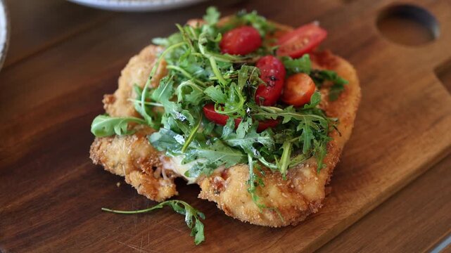 Crispy breaded chicken schnitzel topped with fresh arugula cherry tomatoes balsamic glaze and parmesan served on a wooden board as a gourmet restaurant meal
