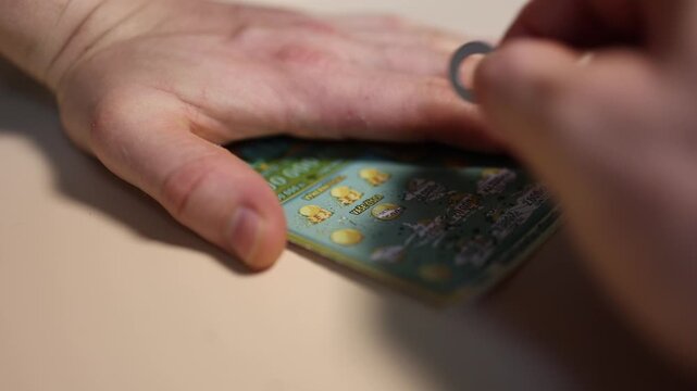 Close up of hands scratching a lottery ticket with a coin hoping to reveal a winning combination claim a jackpot and experience the thrill of luck
