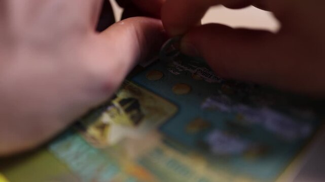 Close up of a hand scratching a lottery ticket with a coin revealing hidden symbols chasing a jackpot testing luck and hoping for an instant cash prize
