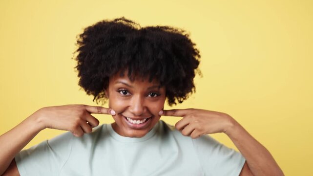 Young african american woman showing her dimples on yellow background