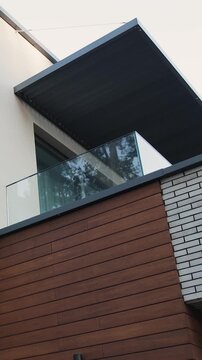 Vertical video. Contemporary house exterior with wood facade, glass balcony and modern roof design