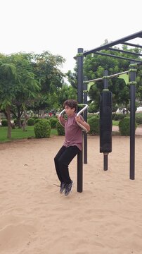 Teenage boy performing dips on parallel bars at an outdoor fitness park. Active adolescent doing bodyweight strength training in a public sports area surrounded by greenery. Healthy lifestyle, youth f