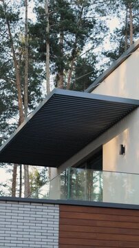 Vertical video. Modern house balcony with slatted roof, glass panels and elegant wood cladding.