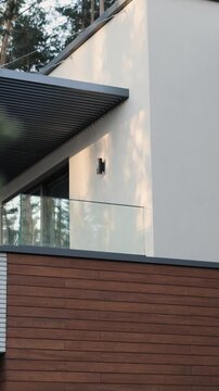 Vertical video. Elegant glass balcony beneath slatted roof on contemporary house surrounded by pines.