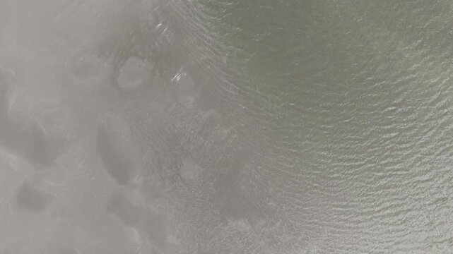 Aerial drone top down shot pushing in over the serene, green-hued waters and sandy shore of a remote fjord beach on the Faroe Islands, showcasing unique patterns in the tidal lagoon.