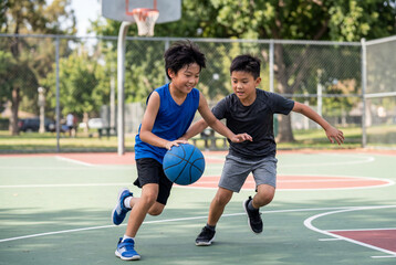 Fototapeta premium Two young asian boys playing a lively game of basketball on an outdoor court