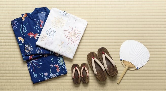 Flat lay of traditional Japanese yukata and geta sandals on tatami mat. Summer festival clothing and paper fan composition