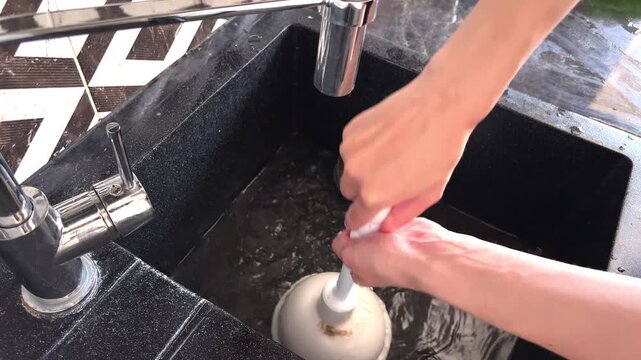 Person's hands using a white rubber plunger to clear a slow kitchen sink drain